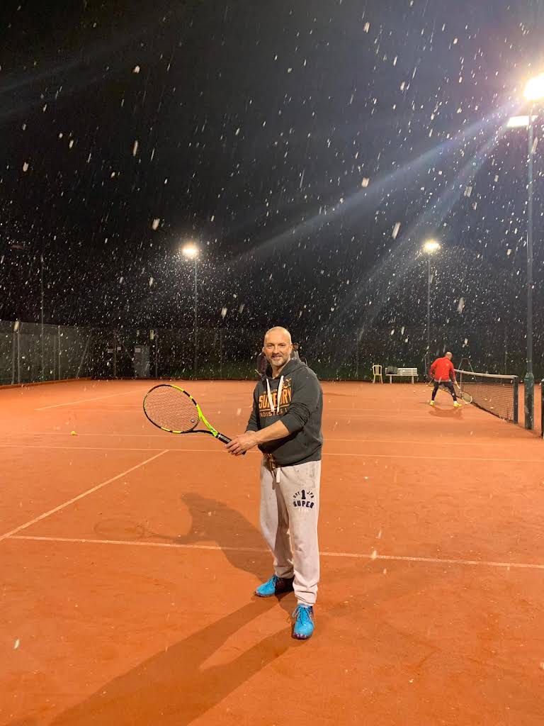 Winter tennis under floodlights with snow flurries
